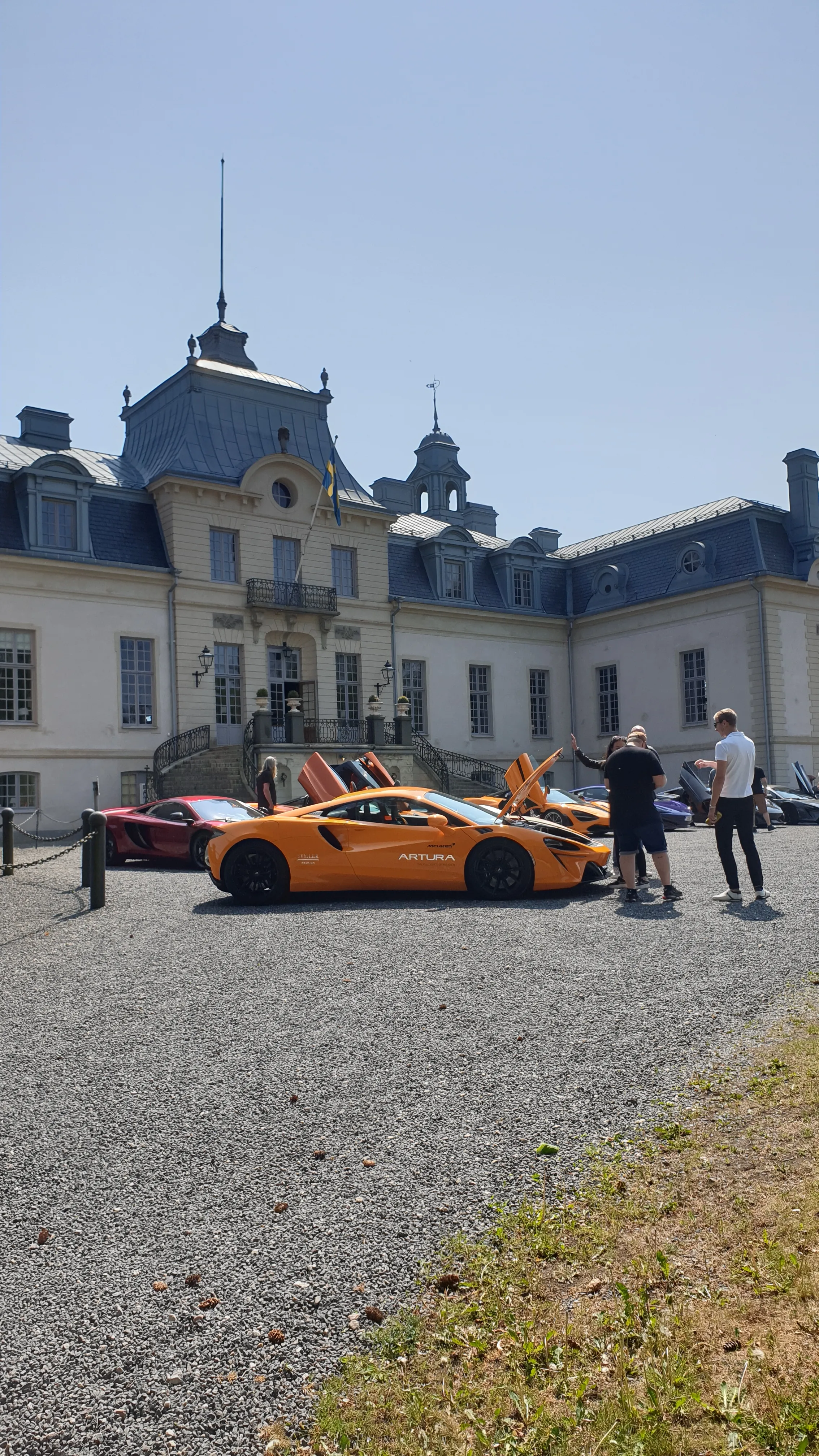 Människor samlade kring flera McLaren-bilar framför en slottsbyggnad.
